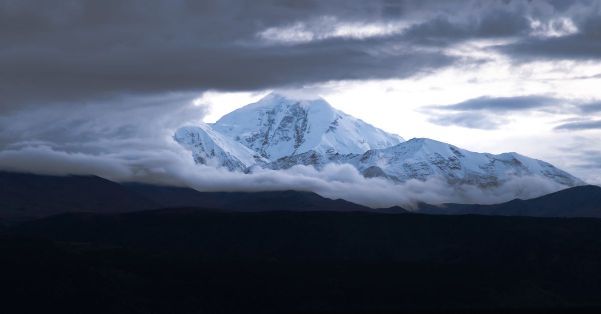 A stunning view of Denali Peak with clouds parting to reveal its snowcapped summit in Alaska.